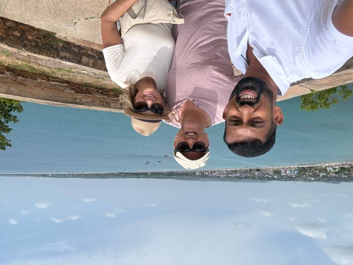 Selfie of guide with two travelers overlooking a wide blue bay and distant town in Sri Lanka.