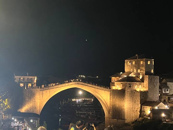 Stari Most bridge in Mostar illuminated at night with silhouettes of visitors along the span