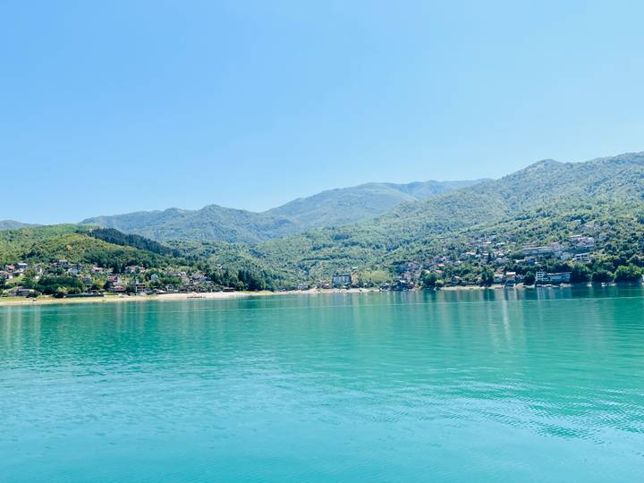 Expansive turquoise lake with surrounding forested hills and small settlements on the shore