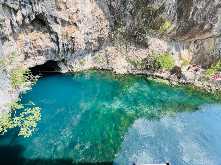 Wide view of the emerald Buna Spring pool with visitors standing on rocks near the water
