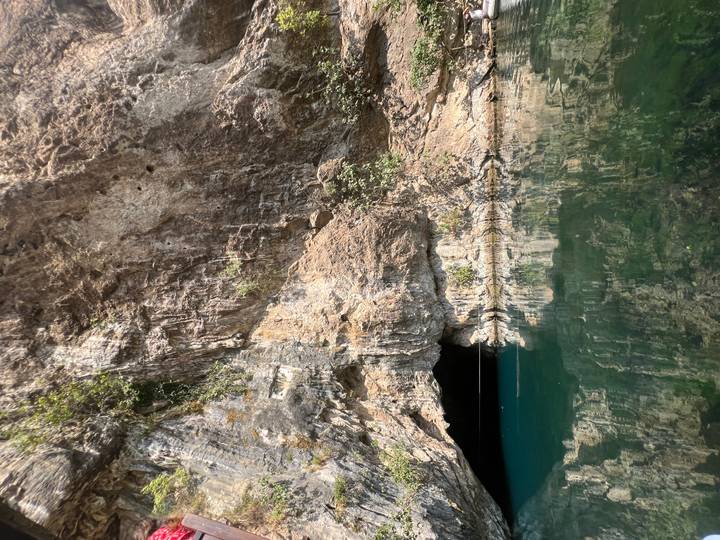 Vertical cliff face above reflective green water at the Buna river source