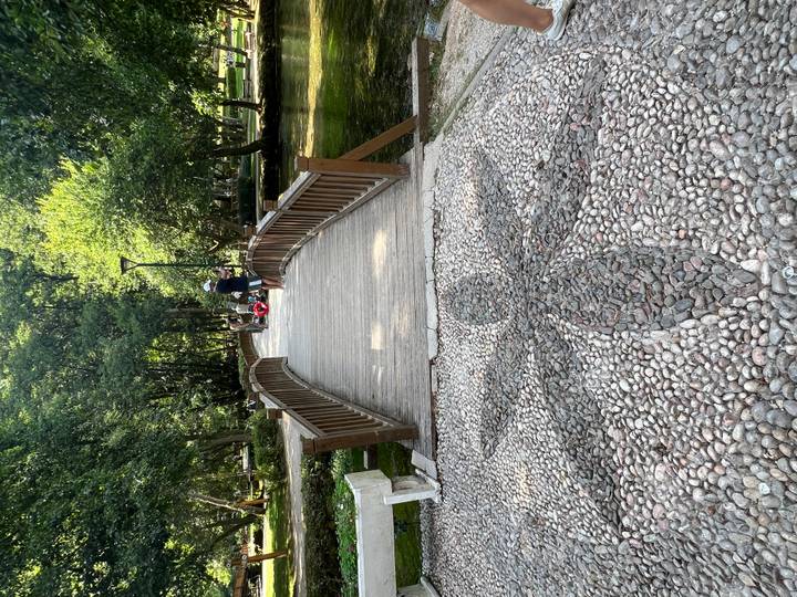 Wooden footbridge over a stream in a shady park with visitors strolling