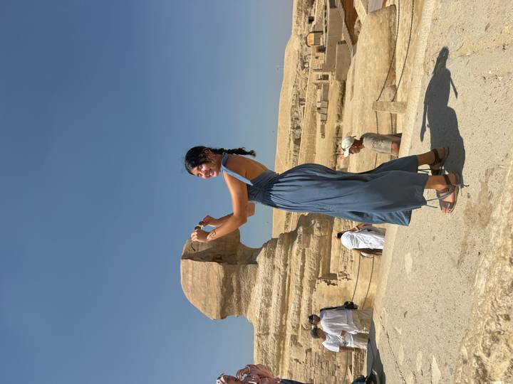 Woman pretends to kiss the Great Sphinx while standing on a viewing platform in bright sunlight