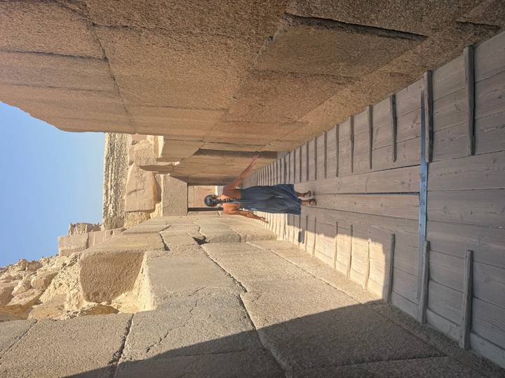 Woman in a blue dress walks down a narrow wooden ramp between towering ancient stone walls
