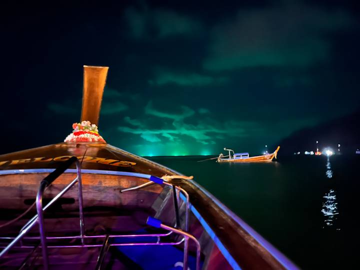 Nighttime long-tail boat ride with glowing green bioluminescent waters and distant fishing boats
