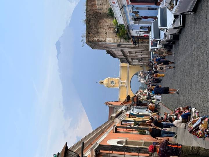 Cobblestone street of Antigua leads to the iconic yellow Santa Catalina Arch with looming volcano backdrop and bustling vendors.