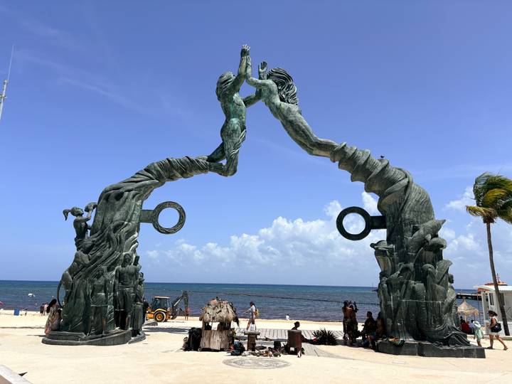Seaside sculpture Portal Maya forms an arch of two bronze figures high-fiving above Caribbean waves in Playa del Carmen.