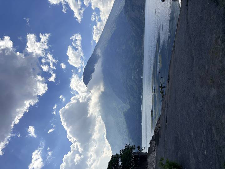 Cloud-capped volcano rises above the calm blue waters of Lake Atitlán under a dramatic sky.