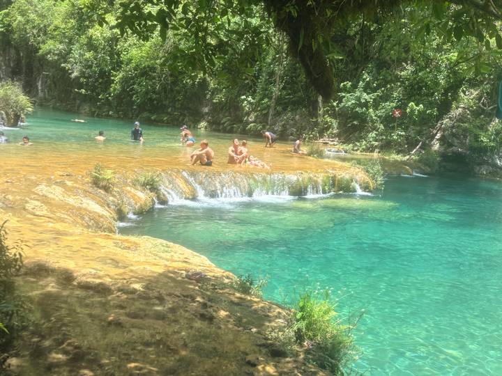 Visitors swim and relax in vivid turquoise tiered pools surrounded by lush jungle foliage.