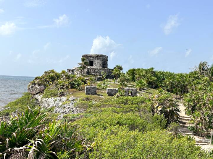 Stone Mayan ruin perched atop a coastal cliff surrounded by jungle with the Caribbean Sea below.