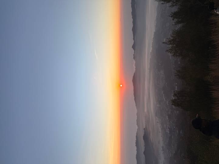 Orange sun rises above mist-filled valley and layered volcanic peaks under a clear gradient sky.