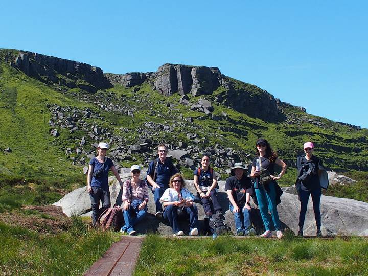 hiking group posing on rocks below a green mountain ridge strewn with boulders