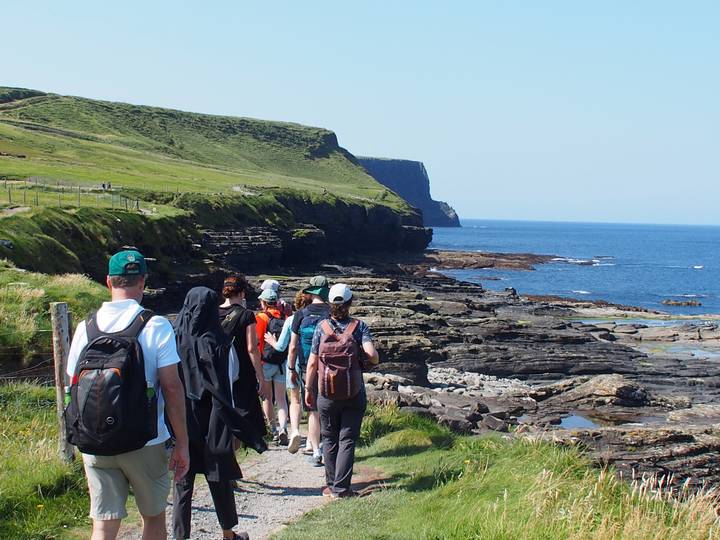 hikers follow a coastal path above dramatic rocky shoreline and blue Atlantic waters