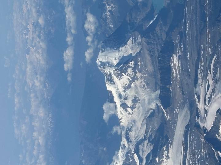 aerial view of a snow-capped mountain peak rising above glaciers and clouds