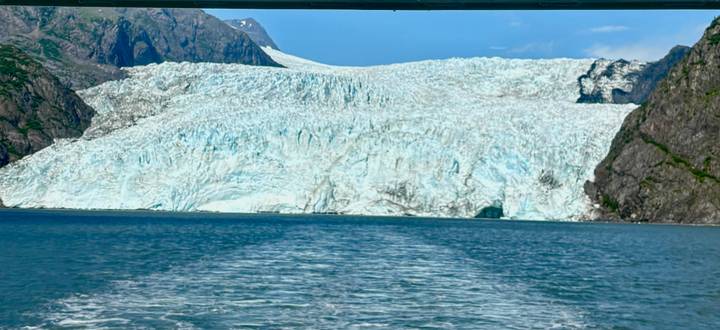 Huge tidewater glacier meeting the turquoise sea with boat wake in the foreground on a bright day