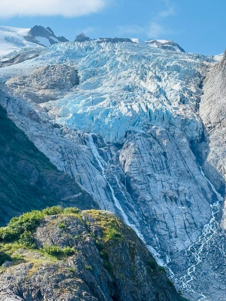 Close-up of a blue glacier face with multiple icy waterfalls cascading down rugged rock
