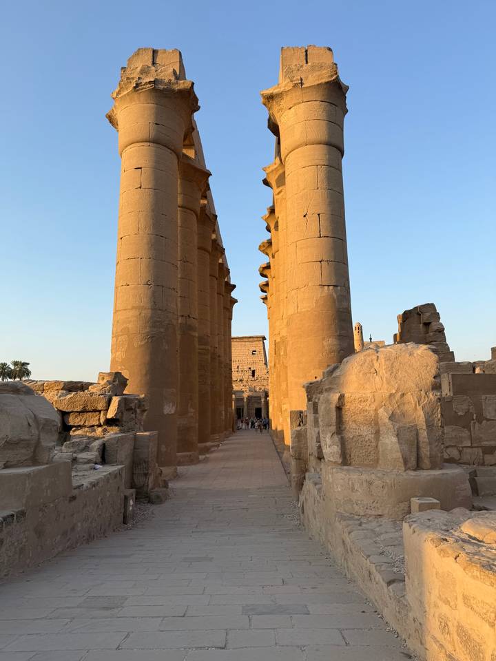 Massive sandstone columns of Luxor Temple glowing in late afternoon light with visitors walking between them