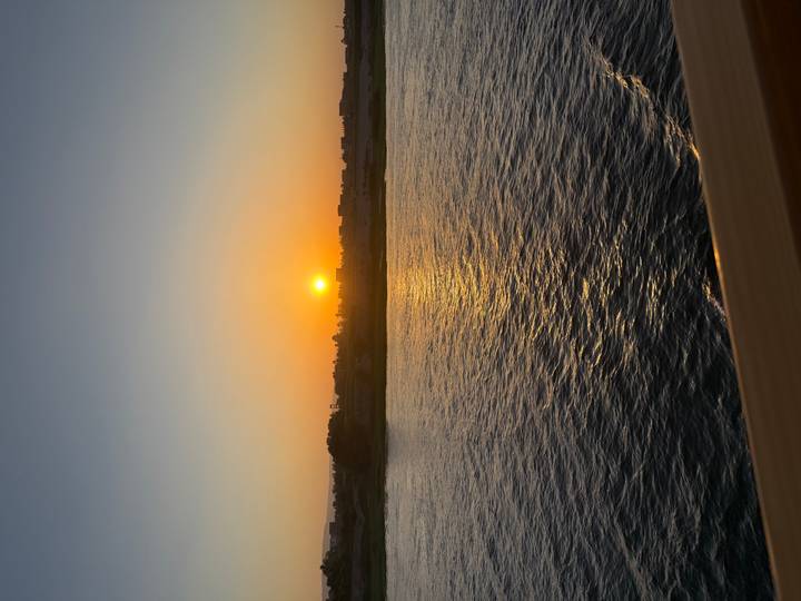Orange sun setting over a distant shoreline casting reflections across calm river waters