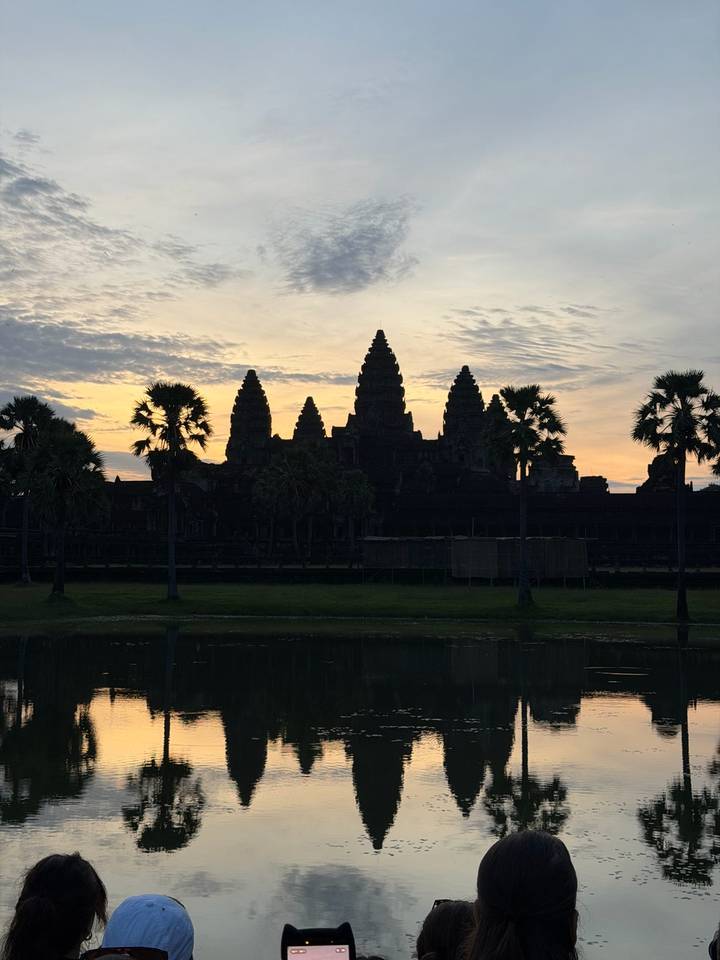 Silhouetted towers of Angkor Wat at dawn behind palm trees reflected in a still pond