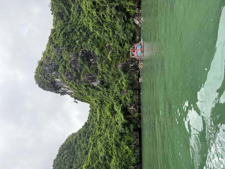 Green limestone karst cliffs rising above emerald waters with a small colorful floating structure