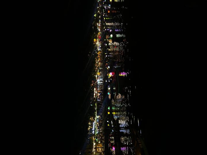 Row of colorful paper lanterns reflecting on a river at night in a lively market town