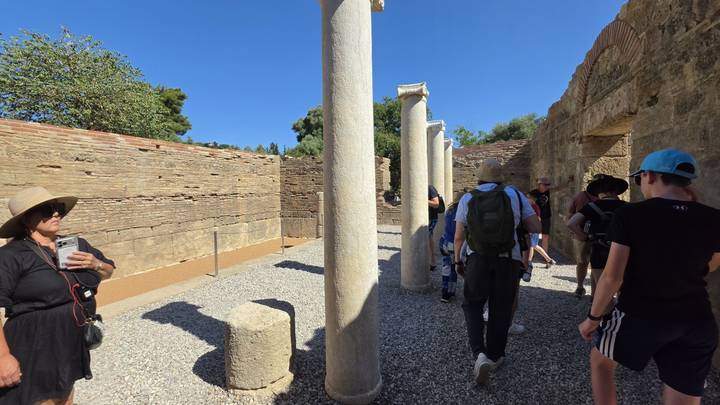 Tourists walk between marble columns and ancient walls inside an archaeological site.