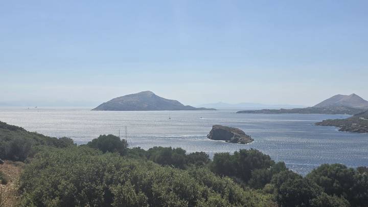 Peaceful coastal view of blue waters dotted with small islands beyond green hills.
