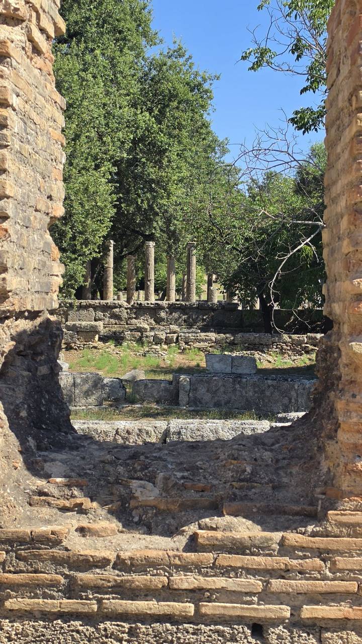View through stone walls toward scattered ancient columns surrounded by greenery.