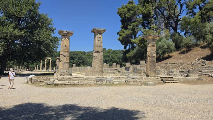 Ruined columns and stone bases stand in an open archaeological area under clear skies.
