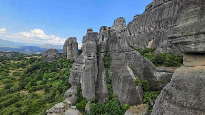 Dramatic vertical cliffs and rock spires of Meteora dominate the verdant landscape below.
