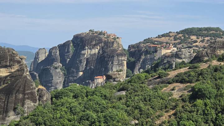 Panoramic view of Meteora monasteries perched atop massive cliffs surrounded by green valleys.