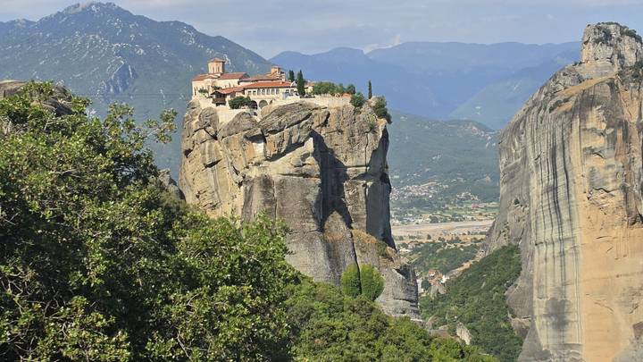 A solitary Meteora monastery crowns a towering rock pillar overlooking valleys and distant mountains.