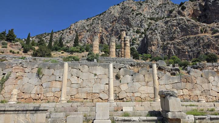 Broken columns of the Temple of Apollo stand against a steep rocky backdrop at Delphi.