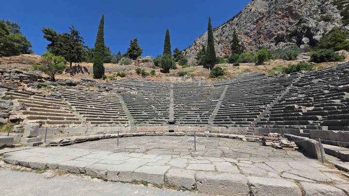 Stone seating tiers of the Ancient Theatre of Delphi curve around the orchestra with a cliff backdrop.
