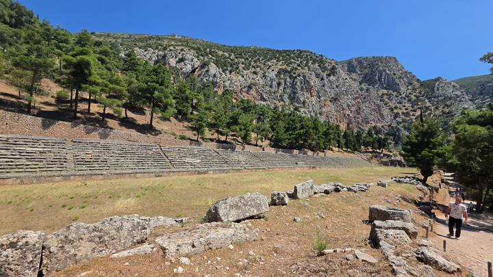 Long rectangular ancient stadium at Delphi set against rocky hills and pine-covered slopes.