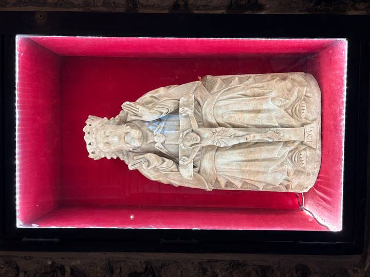 Intricately carved religious statue displayed in a red velvet-lined glass case