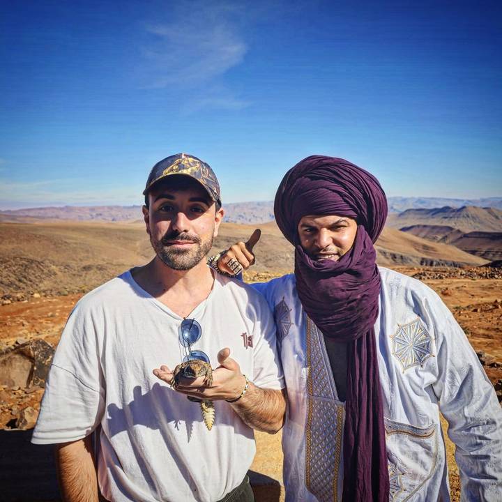 Tourist posing with local Berber guide against a backdrop of arid Moroccan mountains