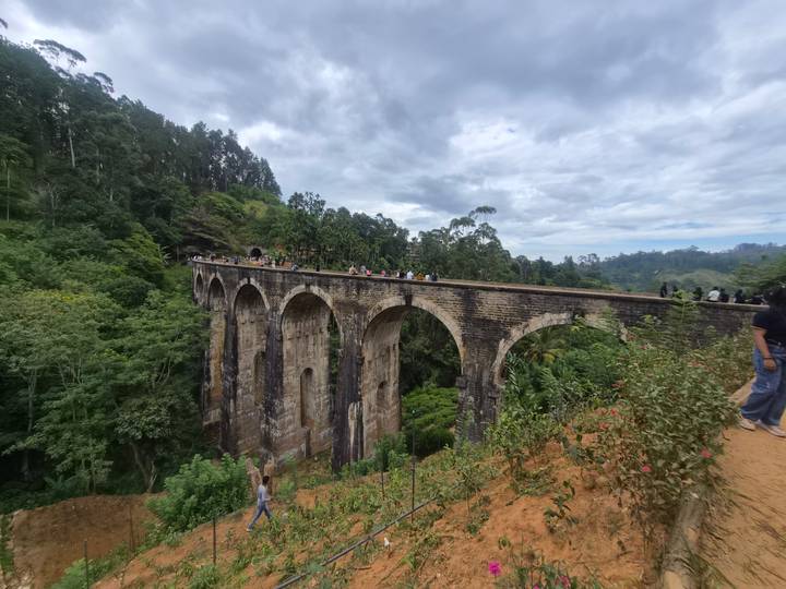Historic Nine-Arch Bridge spanning a lush green valley with visitors walking along its stone arches.