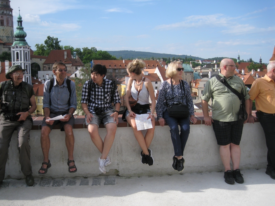 Groupe de touristes assis sur un mur, surplombant une ville européenne.