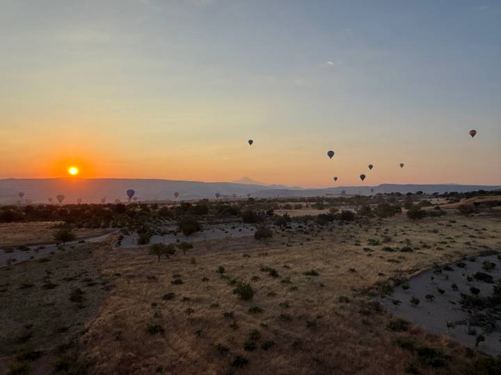 Hot-air balloons drift over Cappadocia’s golden grasslands at sunrise.