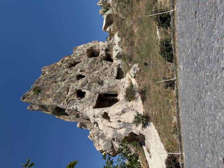 Eroded rock outcrop with ancient cave dwellings and openings against a deep blue sky.
