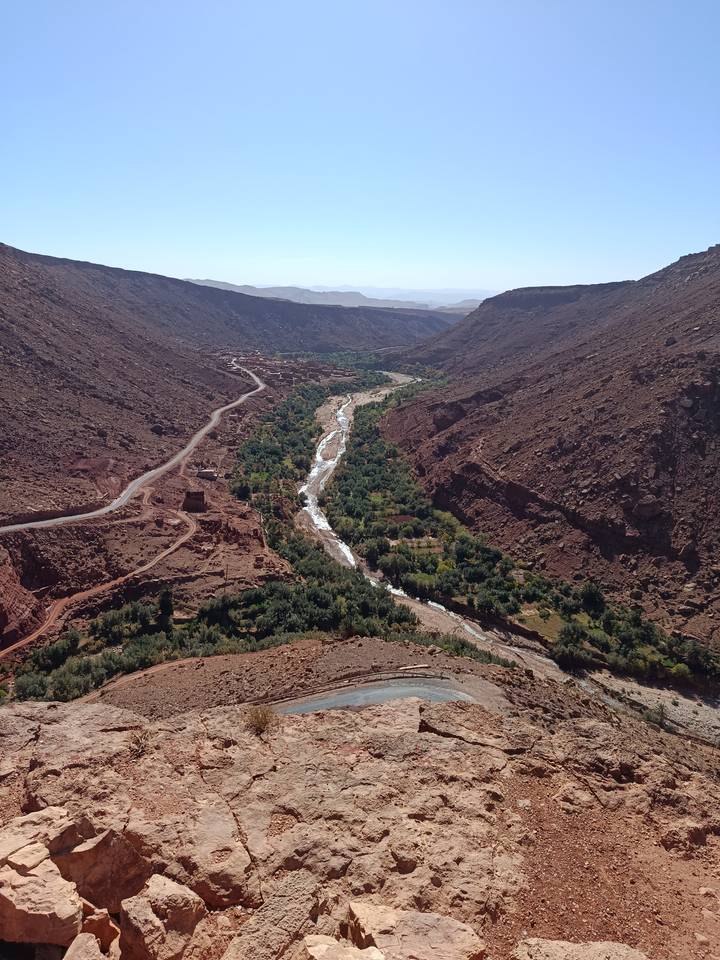 Dramatic red-rock canyon with a winding river and oasis of green villages flanked by rugged mountains.