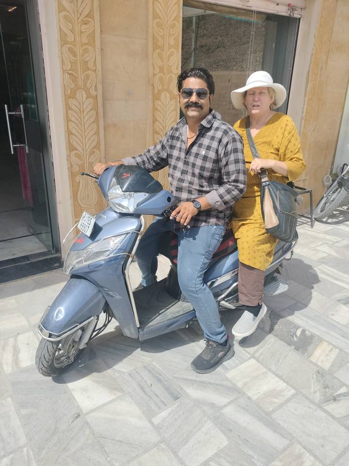 Two people sharing a scooter ride on a sunlit street, close-up on the riders and vehicle.