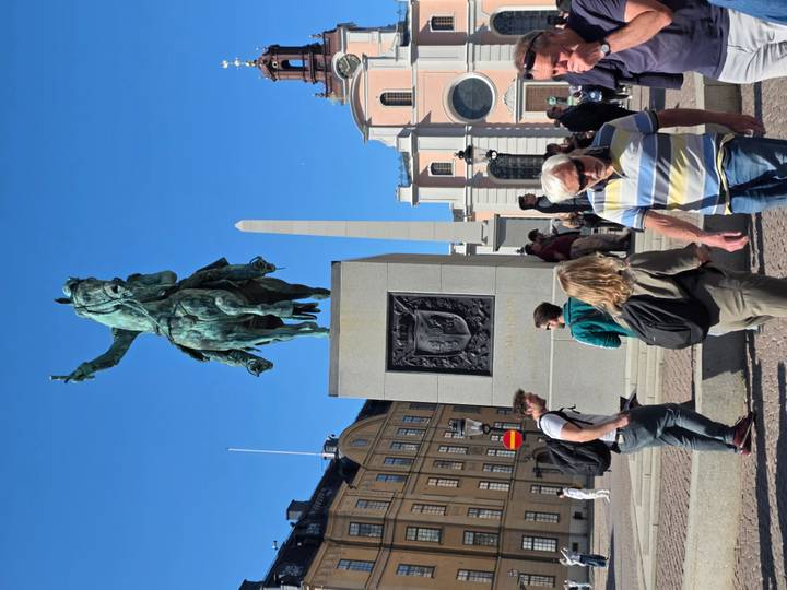 Vertical shot of an equestrian statue on a pedestal in a bustling city square with clear blue sky.