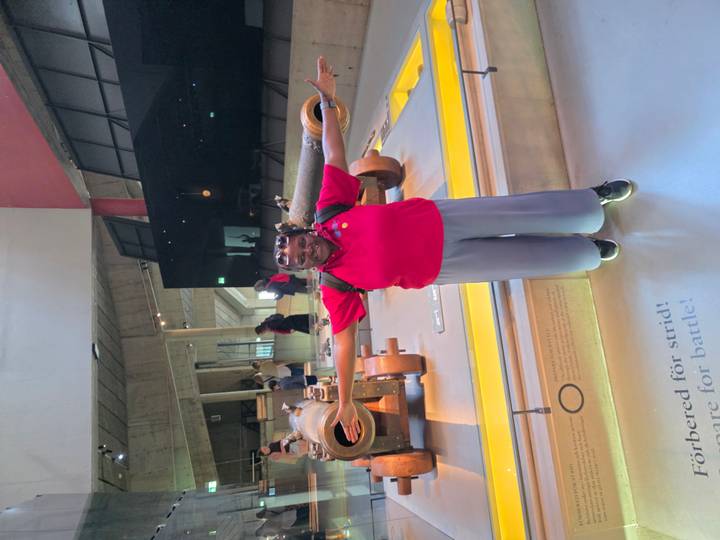 Visitor with arms spread inside a museum hall featuring historic cannons and interactive exhibits.