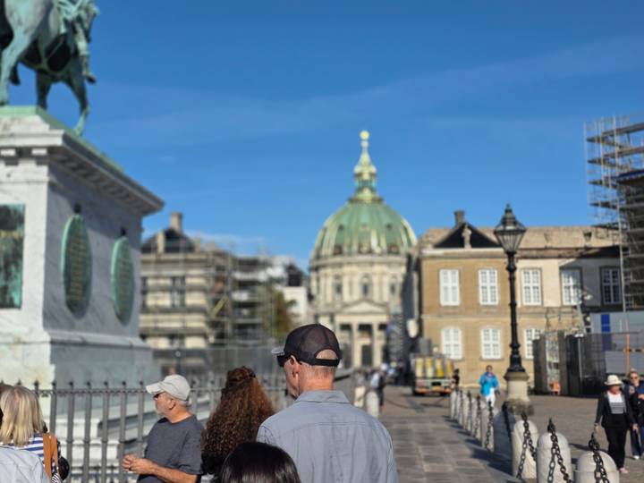 Crowd gathered near an equestrian statue with the green copper dome of Frederik's Church behind.