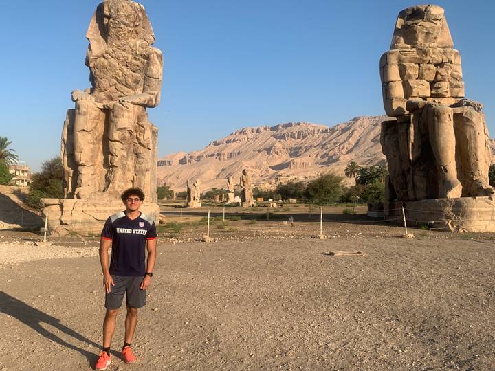 Traveler stands before the towering Colossi of Memnon with desert mountains behind