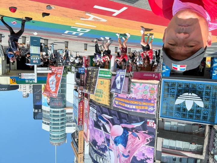 Busy urban crosswalk decorated with rainbow colours and large advertising screens