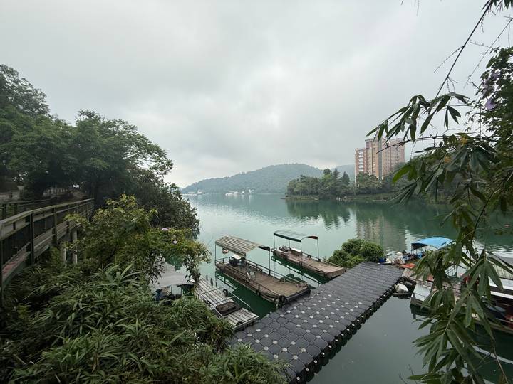 Serene lake with moored boats and forested hills in misty weather