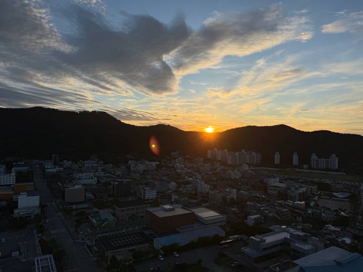 Sunset over city blocks with dramatic clouds and sun dipping behind hills